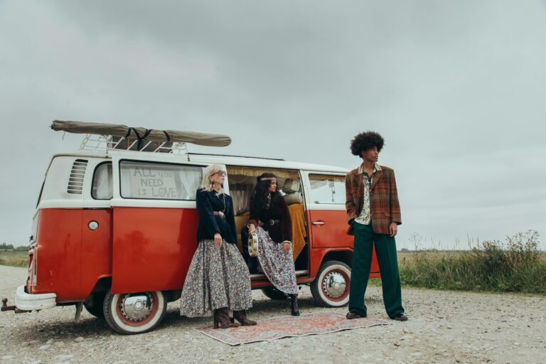 Three adults in bohemian attire enjoying a retro road trip with a vintage red campervan.