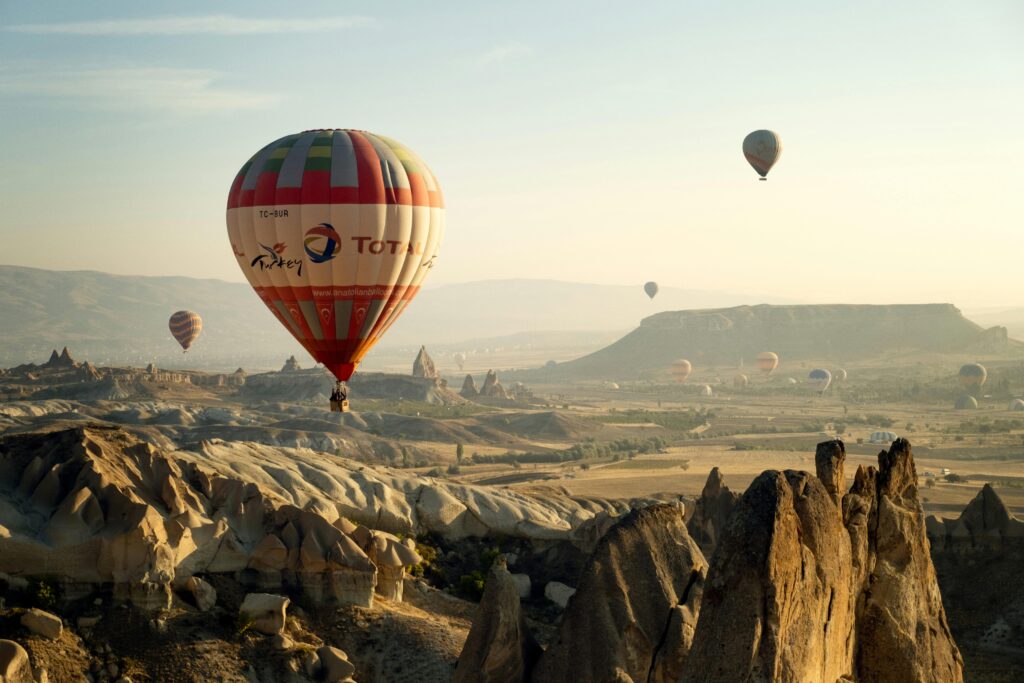 Breathtaking aerial view of hot air balloons floating over Cappadocia's unique rock formations at sunrise.