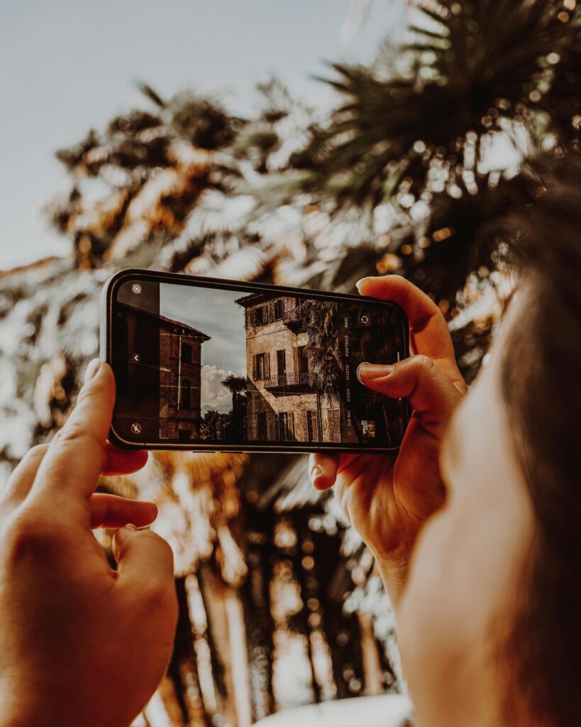 A person photographs historic Stresa building with smartphone, summer feel.